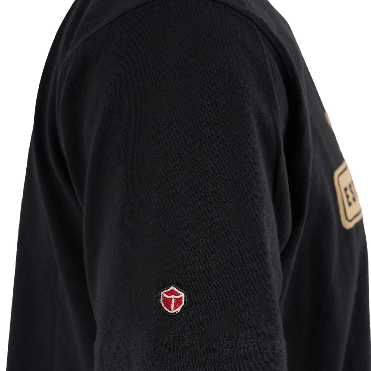 A close-up of a person wearing The Boeing Stores Red Canoe Boeing Defense T-Shirt, a black long-sleeve featuring an embroidered red and white shield emblem on the sleeve near the bicep.