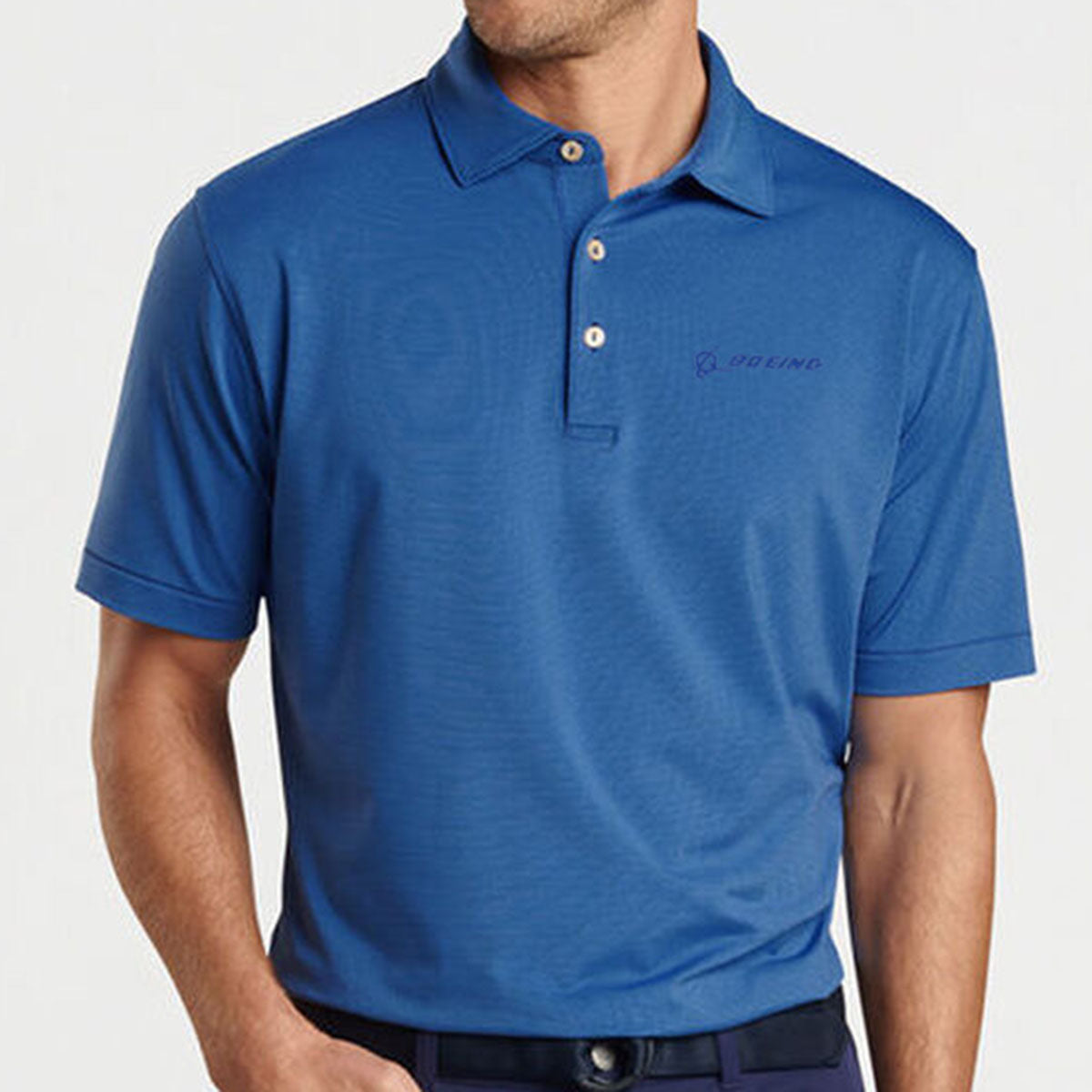 A man wears the Peter Millar Boeing Men’s Jubilee Performance Polo in blue, featuring 4-way stretch, UPF 50+ protection, a collar, buttons, and an embroidered Boeing logo. His face is not visible.