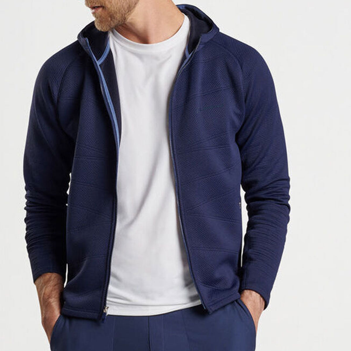 A man stands with his hands in his pockets against a light background, wearing the Peter Millar Boeing Men’s Orion Performance Quilted Hoodie in navy over a white t-shirt and matching navy pants.