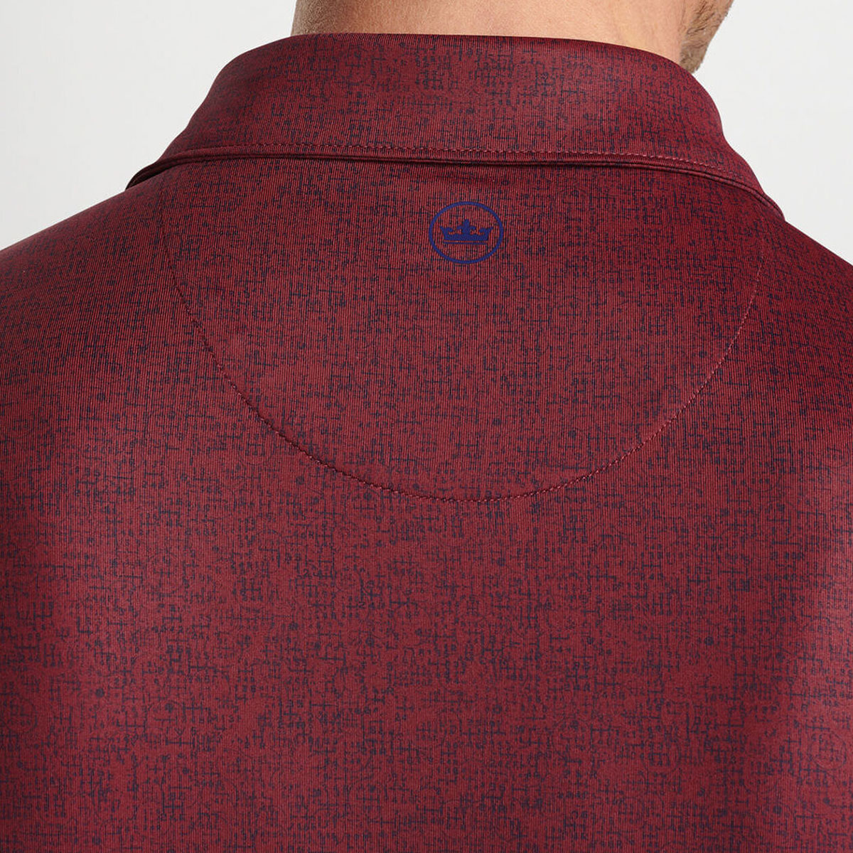 Close-up of the back of a person’s neck and shoulders wearing a maroon textured Peter Millar Boeing Men’s Switching Gears Performance Polo featuring a subtle circular Boeing logo below the collar.