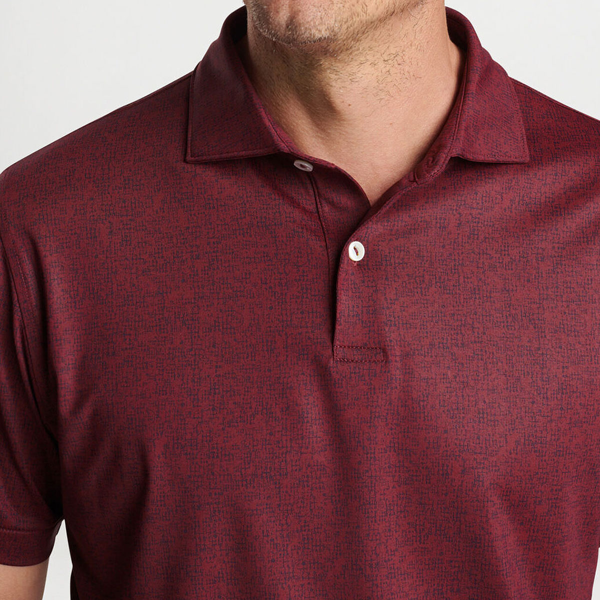 A person wears a maroon Peter Millar Boeing Men’s Switching Gears Performance Polo with a subtle textured pattern, collar, and two white buttons. The performance fabric shirt is from Boeing; the persons face is partially out of frame.