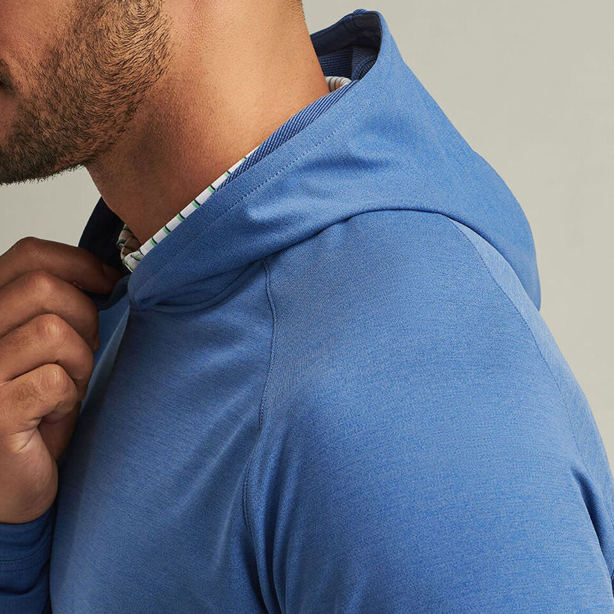 A close-up shows a man wearing the Peter Millar Boeing Men’s Pine Performance Hoodie by BOEING, holding the collar. Only his lower face, neck, and upper torso are visible, emphasizing its comfort and moisture-wicking performance fabric.