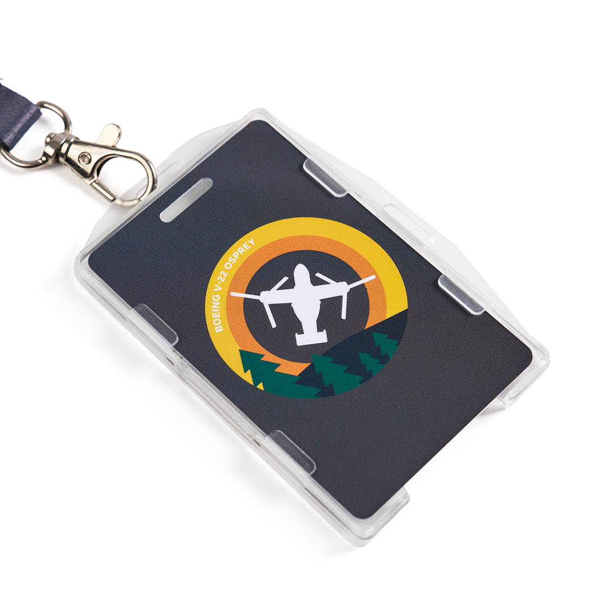 The Boeing V-22 Osprey Skyward Lanyard by Boeing features a clip-on badge displaying a sublimation print of the aircrafts silhouette against a circular yellow-orange backdrop, accented by green trees, all encased in a clear plastic holder.