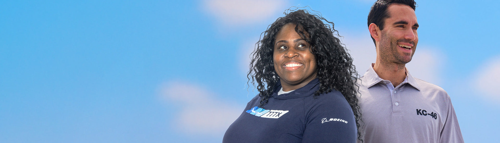 Two individuals wearing Boeing-branded apparel, one in a navy blue shirt and the other in a light gray polo, set against a blue sky background.