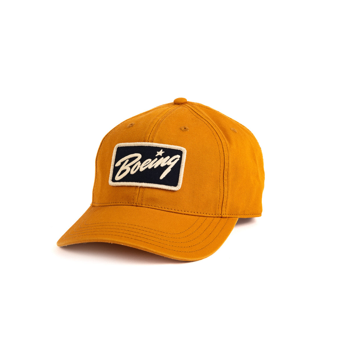 The Boeing Stores Boeing Washed Twill Patch Hat is a mustard yellow baseball cap with a black and white patch that features stylized text. It includes a curved brim, visible stitching, and an adjustable buckle closure for the perfect fit.