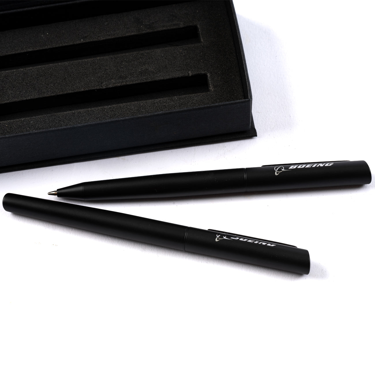 The Boeing Angle Tip Pen Set by The Boeing Store features two stylish black ink pens with Boeing branding, displayed next to an open black case with pen-shaped slots on a white surface for a sleek, sophisticated look.