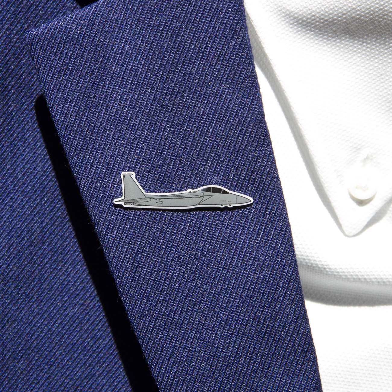 A close-up shows a person in a navy suit jacket adorned with The Boeing Stores silver-tone F-15 lapel pin. The gray fighter jet design enhances the sleek look, complemented by the visible buttons on the white shirt beneath.