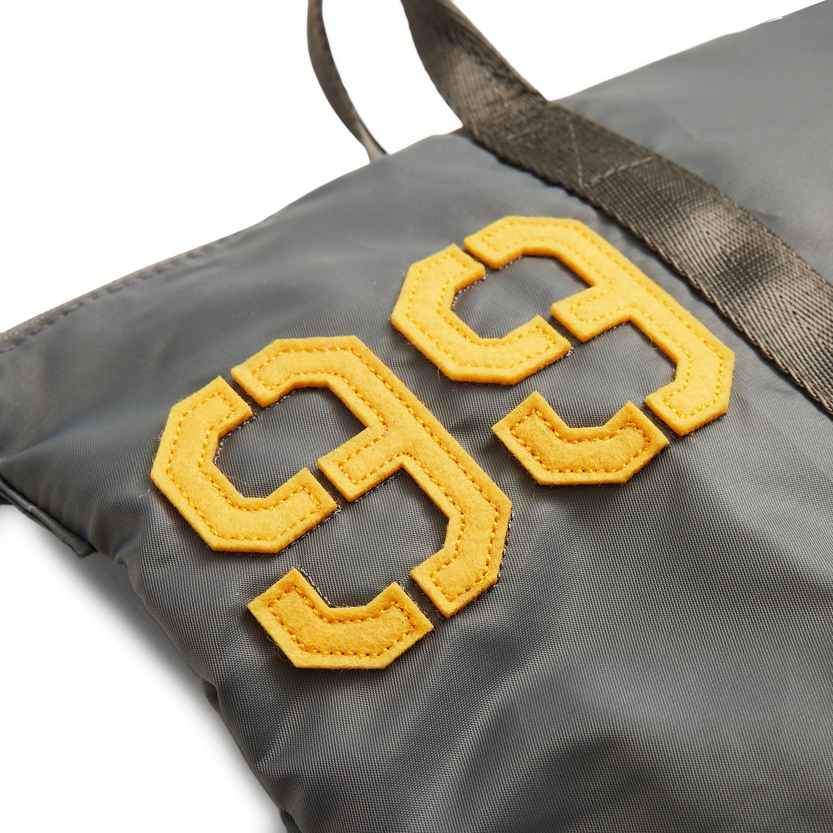 The Boeing Stores Red Canoe Tuskegee Helmet Bag features a close-up of a gray bag with shiny fabric and yellow 99 patches. An adjustable shoulder strap hints at its practicality and style.