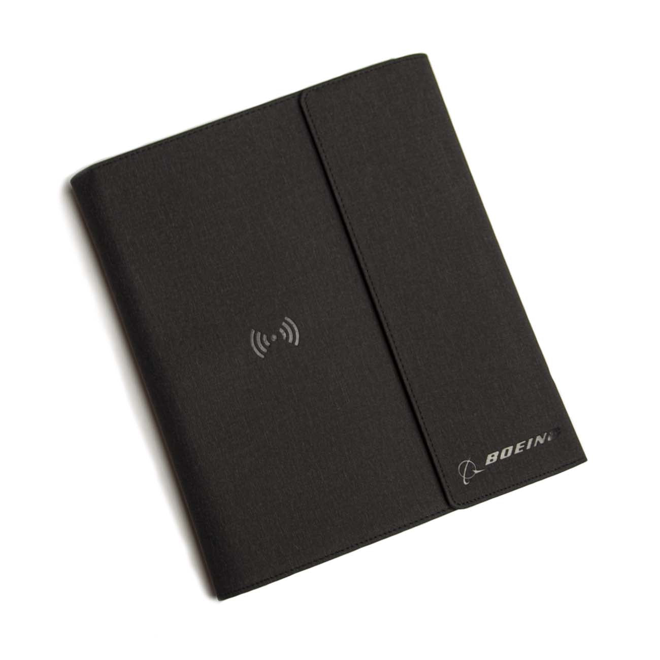 The Boeing Stores sleek, black faux leather Boeing Large Padfolio With Wireless Power Bank boasts a magnetic flap, wireless charging symbol in the center, and a subtle Boeing logo in the bottom-right corner, offering a smooth and professional finish that combines style with functionality.