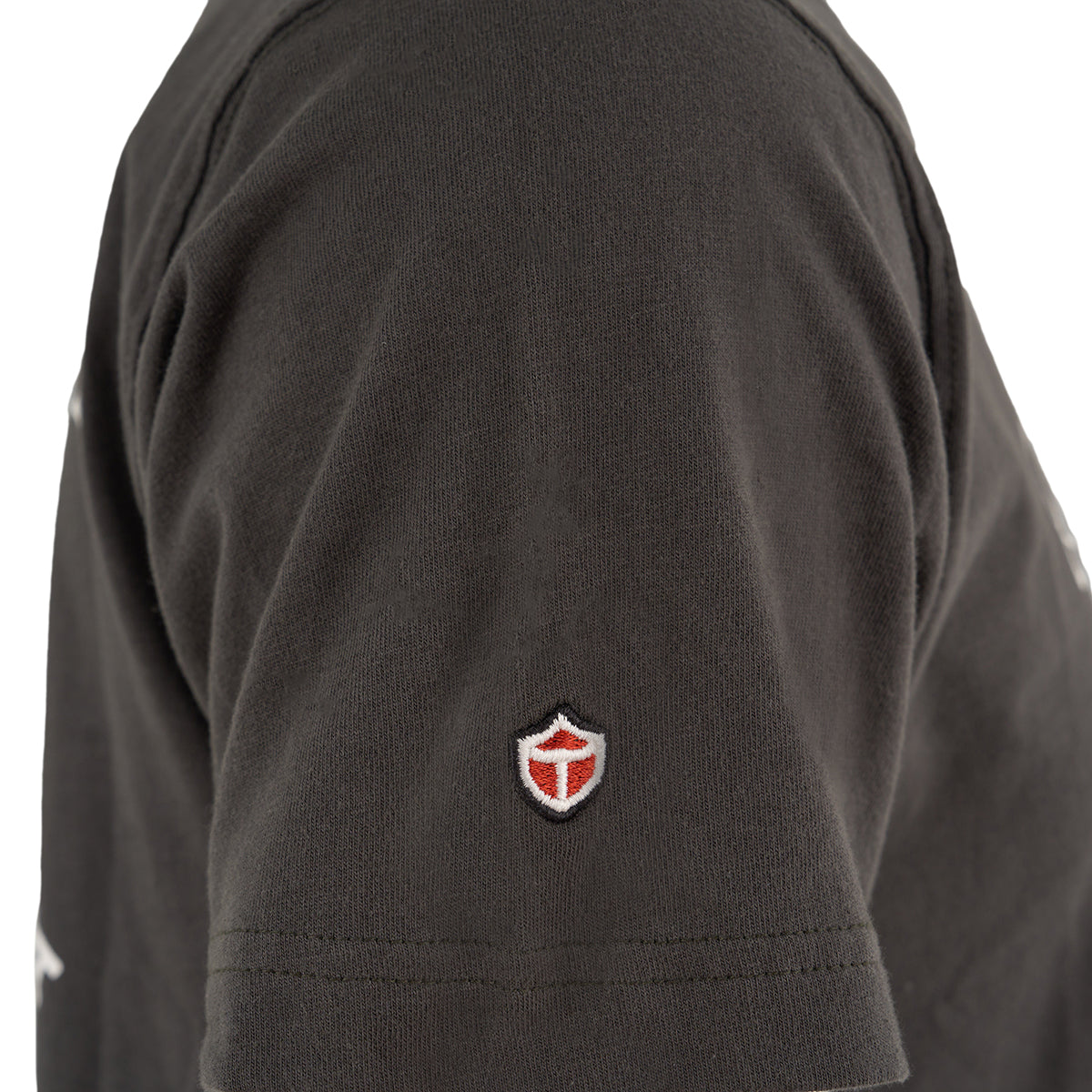 Close-up of the sleeve on a Red Canoe Boeing Company T-Shirt from The Boeing Store, showing a small embroidered red and white shield emblem near the hem.