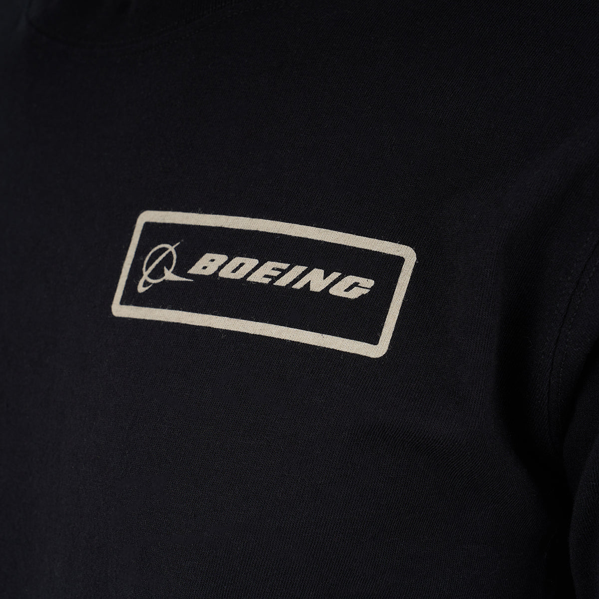 Close-up of The Boeing Store’s Red Canoe Boeing Long Sleeve T-Shirt, featuring a rectangular white patch with the Boeing logo and stylized text on the upper chest.