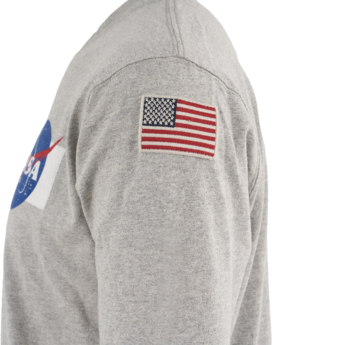 A close-up side view shows a person wearing The Boeing Stores Red Canoe NASA Long Sleeve T-Shirt, made from 100% cotton, with a NASA logo on the chest and an embroidered American flag patch on the upper sleeve.