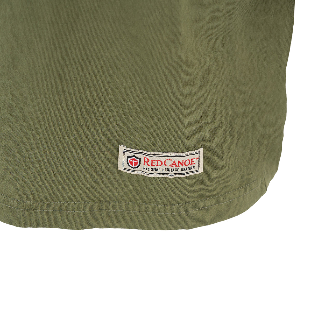 A close-up of an olive-green fabric shows a rectangular patch with a red and black shield logo, the text Red Canoe National Heritage Brands, and tributes to Boeings legacy—a perfect touch for The Boeing Store’s Red Canoe Boeing Airplane Company Logo T-Shirt in any retro tee collection.