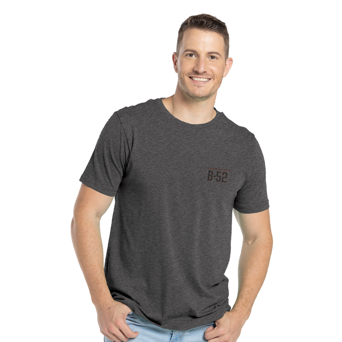 A smiling man confidently stands with his hands in his pockets, wearing a high-quality Boeing B-52 Mens T-Shirt with B-52 Stratofortress on the front against a white background.