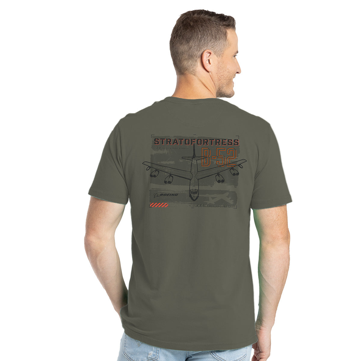 A man in light blue jeans and short hair is wearing a Boeing B-52 Mens T-Shirt by Boeing. This olive green cotton blend tee features a graphic of a B-52 Stratofortress on the back as he faces away, looking to the side.