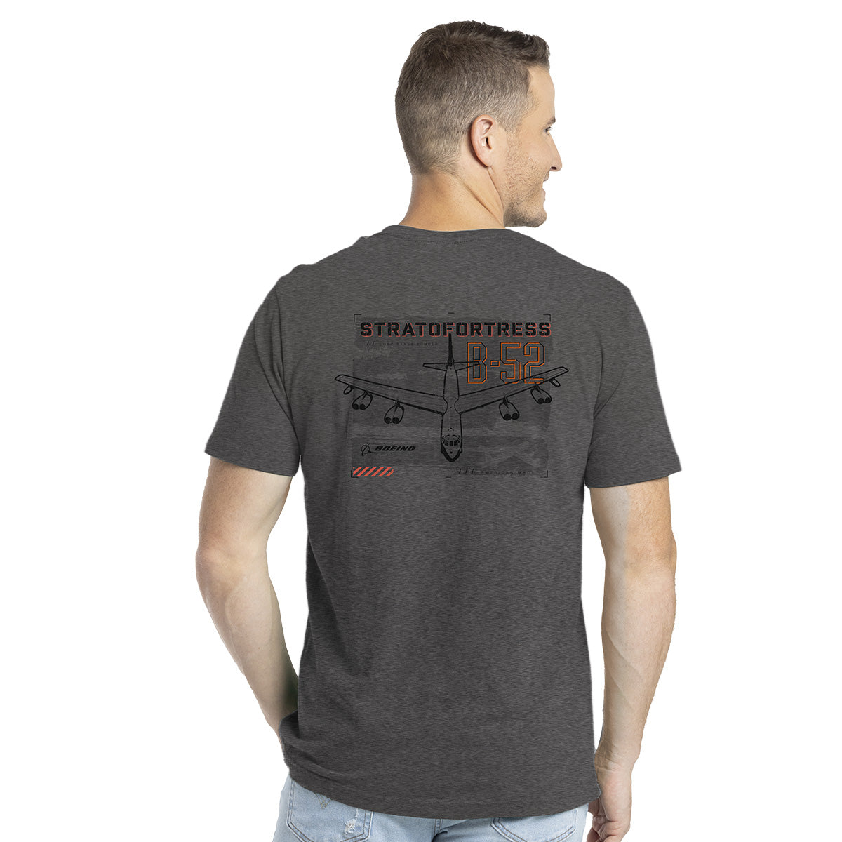 A man in a Boeing B-52 Mens T-Shirt, featuring a B-52 Stratofortress illustration and text on the back, is standing and looking to the side. The gray shirt is made from a high-quality cotton blend.