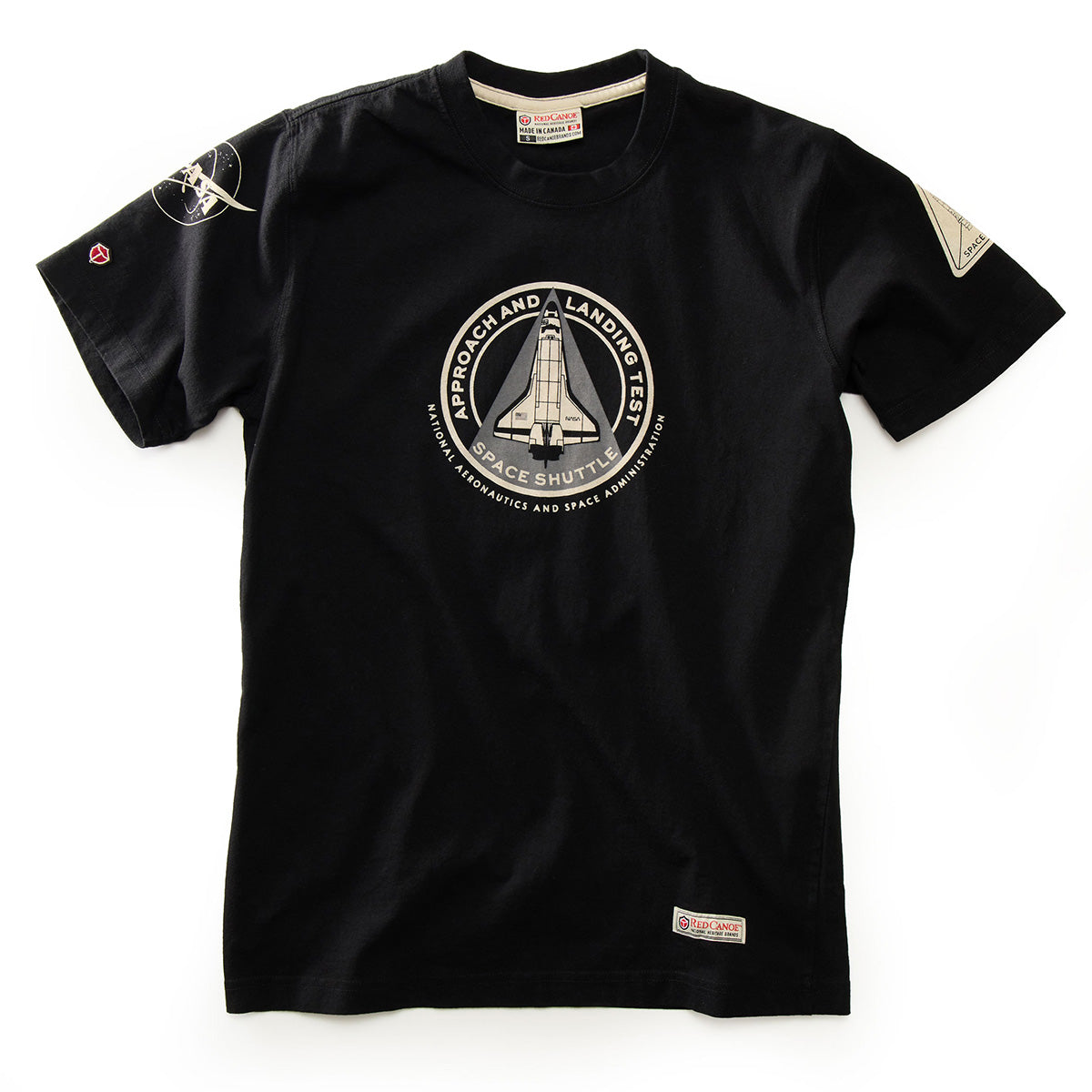 Introducing the Red Canoe NASA ALT T-Shirt by Boeing—a black tee featuring a circular Space Shuttle Approach and Landing Test (ALT) patch on the chest, complemented by additional space-themed patches on the left sleeve and near the hem. This classic, NASA-inspired shirt is perfect for any aspiring astronaut.