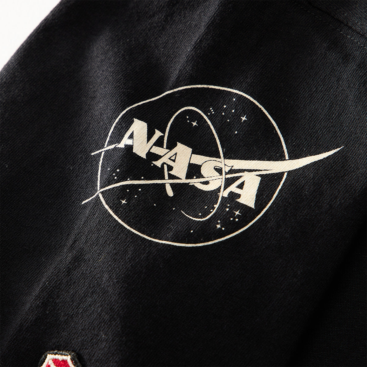 Close-up of the Red Canoe NASA ALT T-Shirt by Boeing, showcasing a white NASA logo with an orbit design and stars printed on black fabric—ideal for any astronaut shirt or NASA-inspired tee collection.