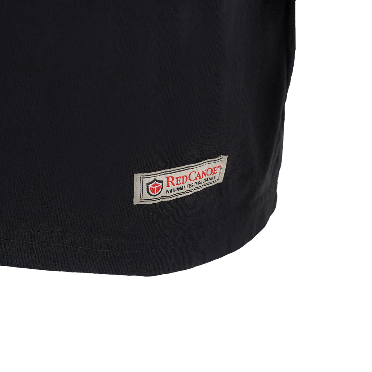 Close-up of the bottom hem of a black Red Canoe NASA ALT T-Shirt by Boeing, showing a small rectangular patch with the “Red Canoe National Heritage Brands” logo in red and white.