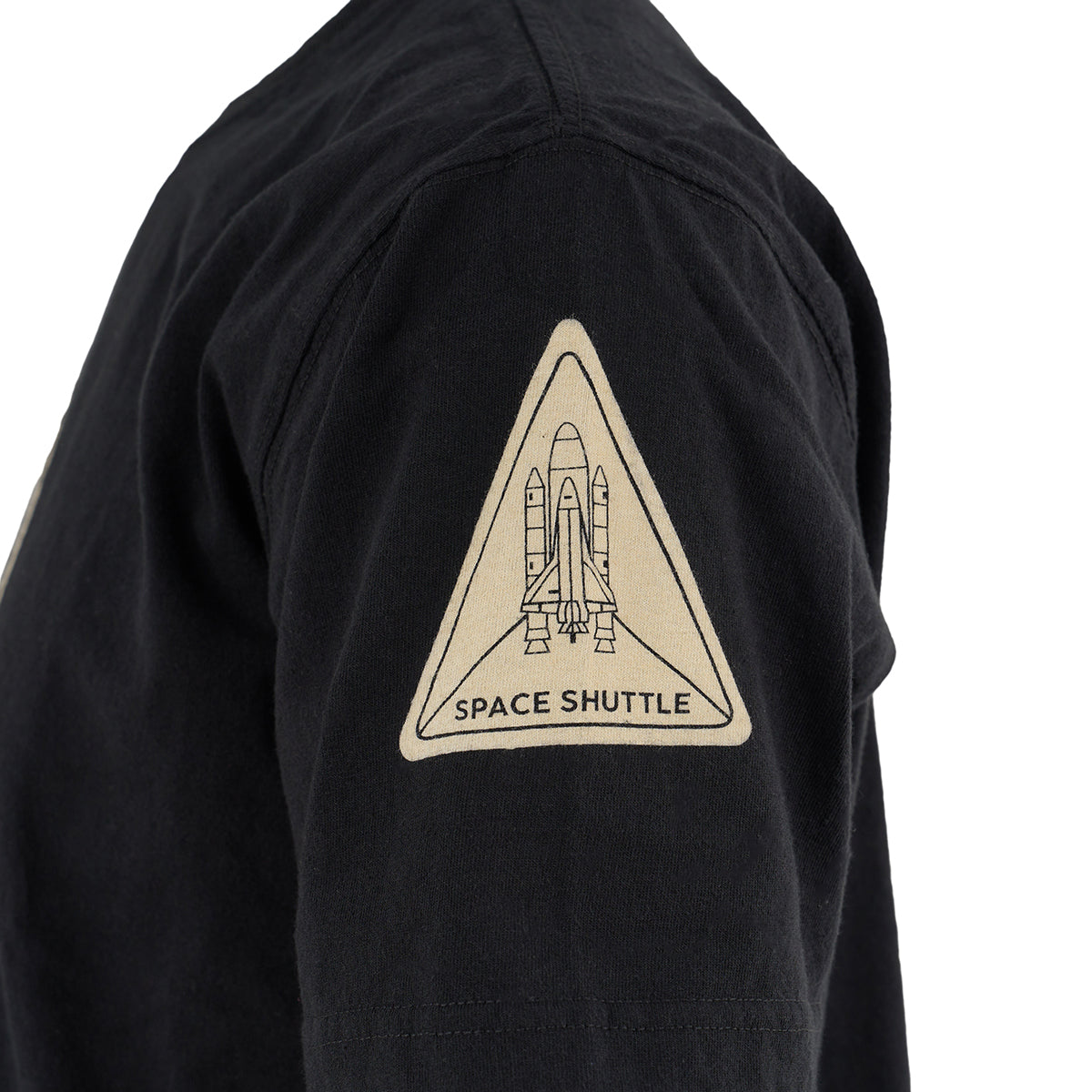 A close-up of the Red Canoe NASA ALT T-Shirt by Boeing shows a black sleeve with a triangular patch featuring a line drawing of a space shuttle and the words Space Shuttle below the image.