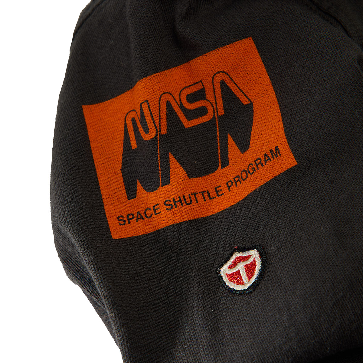 The BOEING Red Canoe Space Shuttle Mens Long Sleeve T-Shirt is black with an orange Space Shuttle Program logo and a small red and white shield patch embroidered below it.