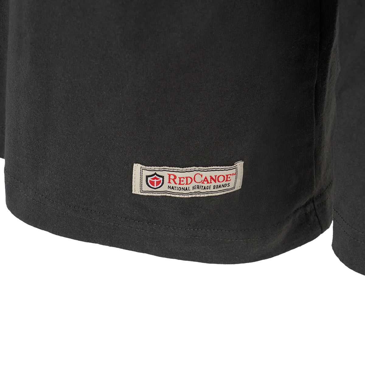 Close-up of the bottom hem of a black Red Canoe Space Shuttle Mens Long Sleeve T-Shirt by BOEING, showing the rectangular fabric label with shield logo—perfect for NASA apparel fans.