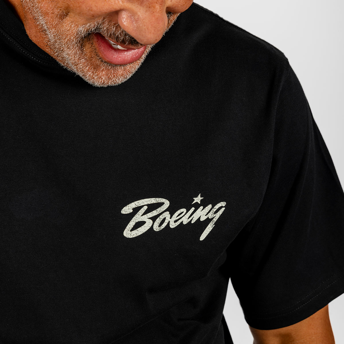 A person wearing the Boeing Heritage Script B-17 Flying Fortress Unisex T-Shirt, featuring the iconic white “Boeing” script logo across the chest, proudly displays their appreciation for aviation heritage. Only the lower face and upper torso are visible.