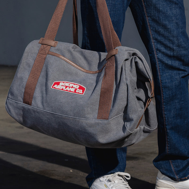 Zoomed in image of a man holding a grey Boeing heritage duffel bag with the Boeing Airplane Co. logo patch on there.