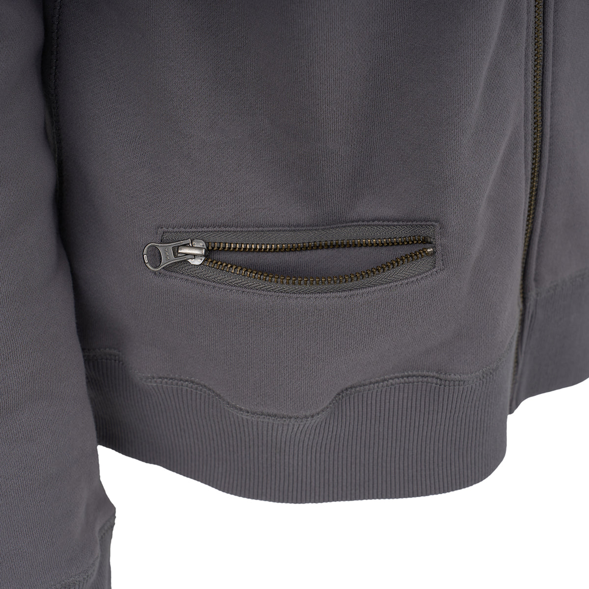 Close-up of the lower half of a Red Canoe Boeing Full Zip Sweatshirt by The Boeing Store, featuring a zippered pocket, ribbed hem, and partially opened metallic zipper. The soft fleece fabric appears smooth and comfortable.