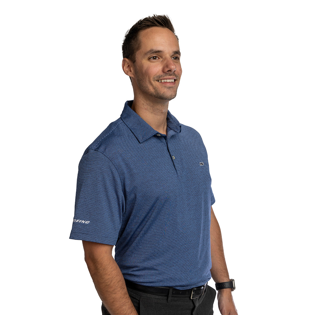 A man with short brown hair smiles against a white background, wearing the Boeing Vineyard Vines Men’s Micro Stripe Polo with moisture-wicking fabric, a small chest logo, “Boeing” on the left sleeve, and classic black pants.