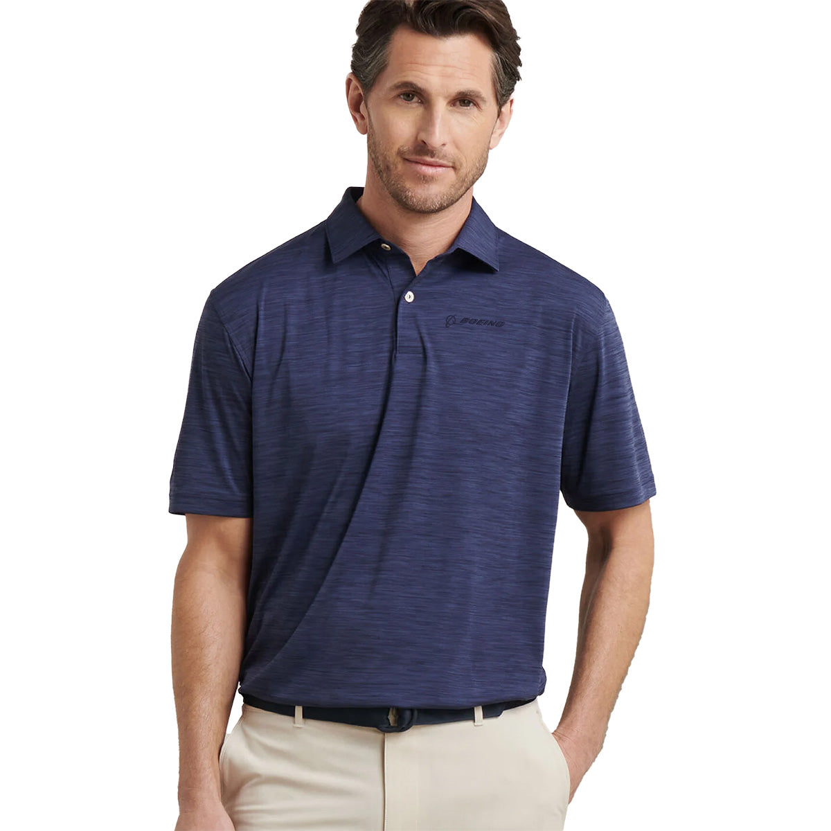 A man with short brown hair wears the BOEING Peter Millar Boeng Men’s Featherweight Mélange Polo and light beige pants, standing with his hands in his pockets against a white background.