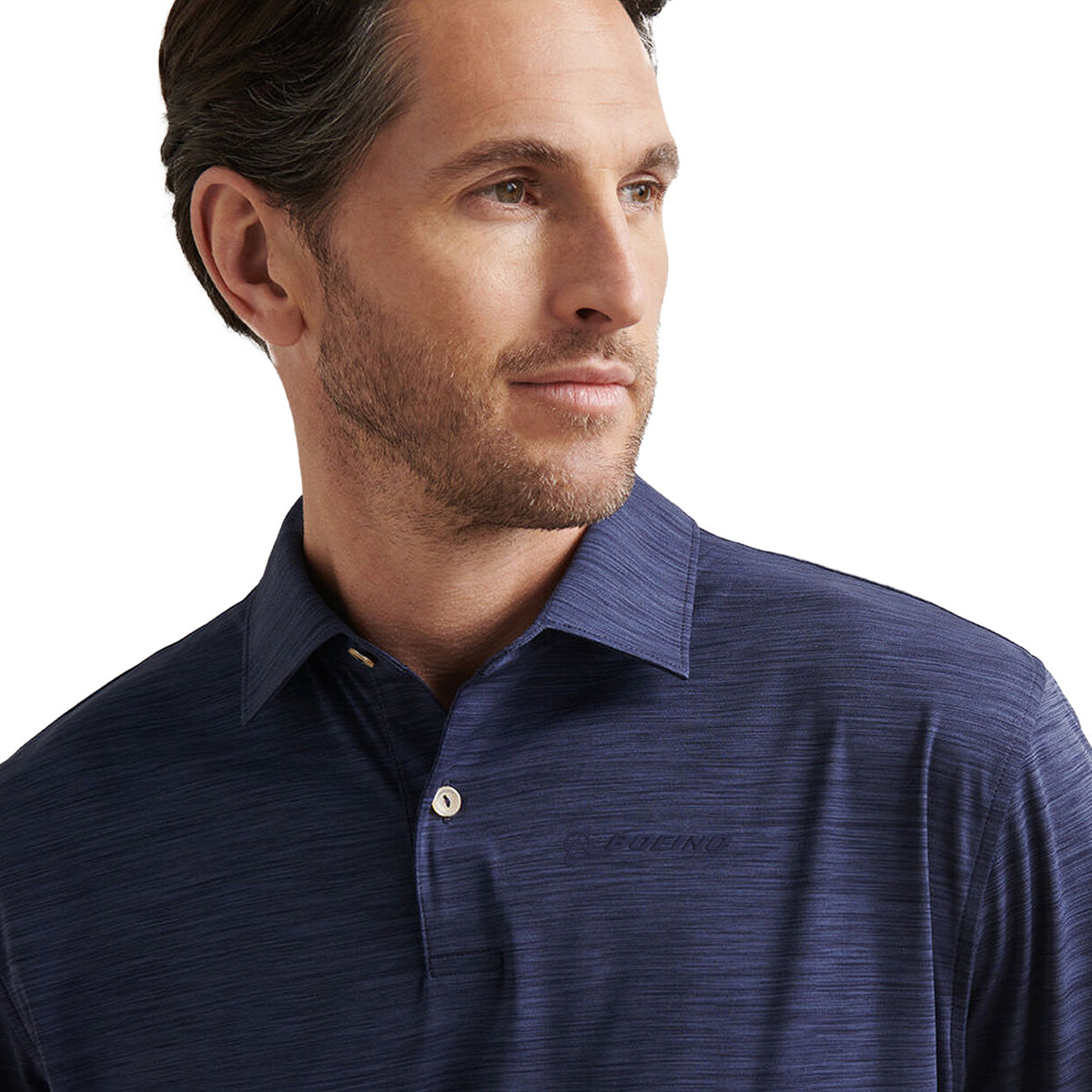 A man with short brown hair and light stubble wears the BOEING Peter Millar Boeng Men’s Featherweight Mélange Polo in dark blue, looking slightly to his right against a plain white background.