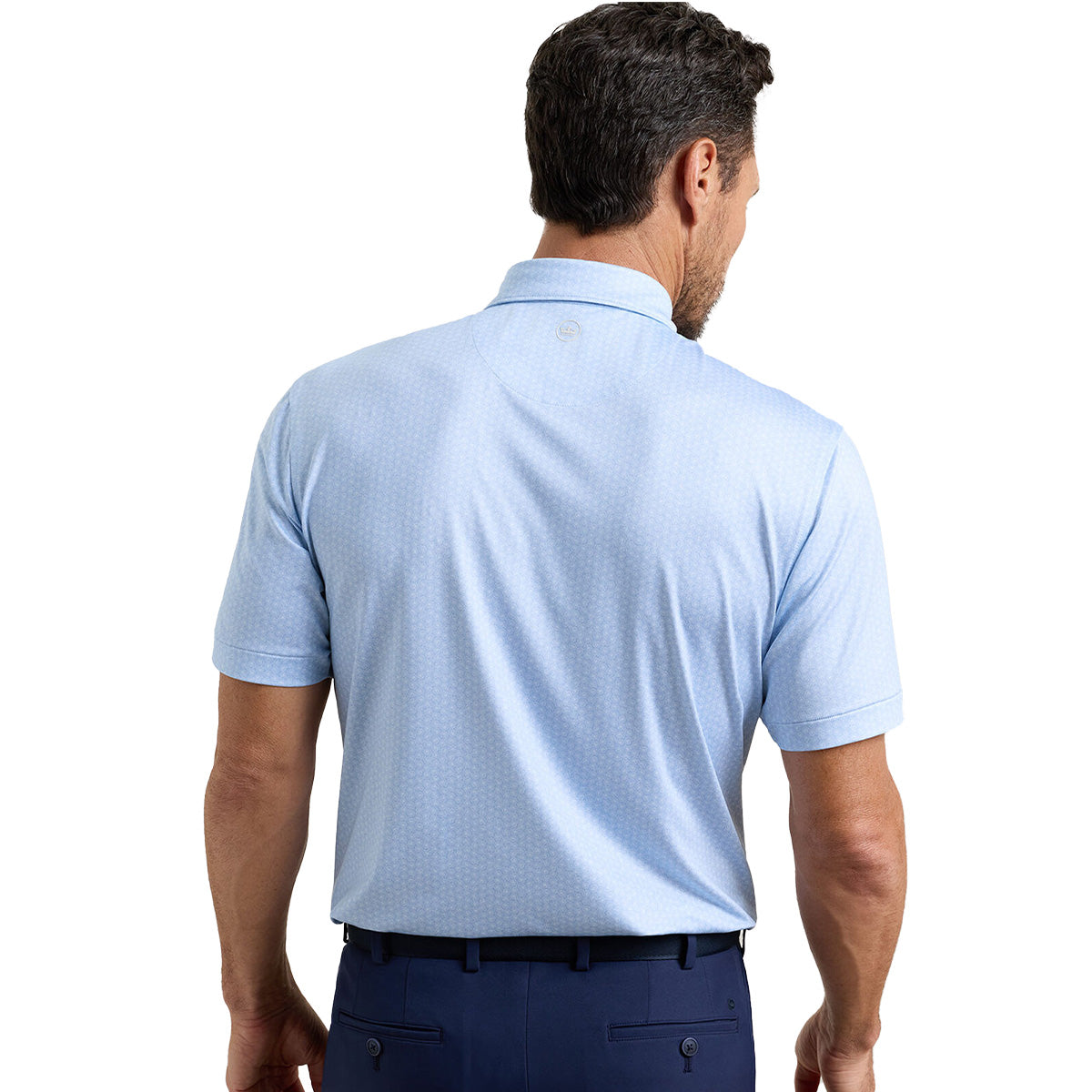 A man stands with his back to the camera, wearing a Peter Millar Boeing Men’s Nautilus Performance Polo by BOEING in light blue, tucked into dark pants. The polo features a subtle pattern, collar, and UPF 50+ for all-day comfort.