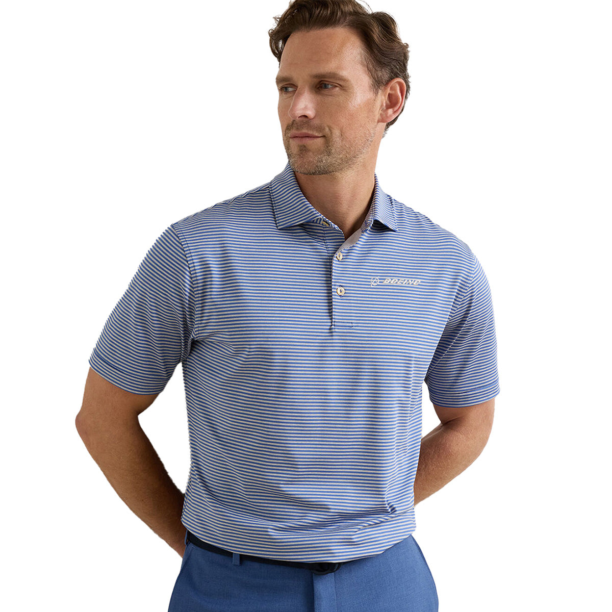 A man wearing a blue and white striped Peter Millar Boeing Men’s Hales Performance Polo stands with his hands behind his back, looking to the side.
