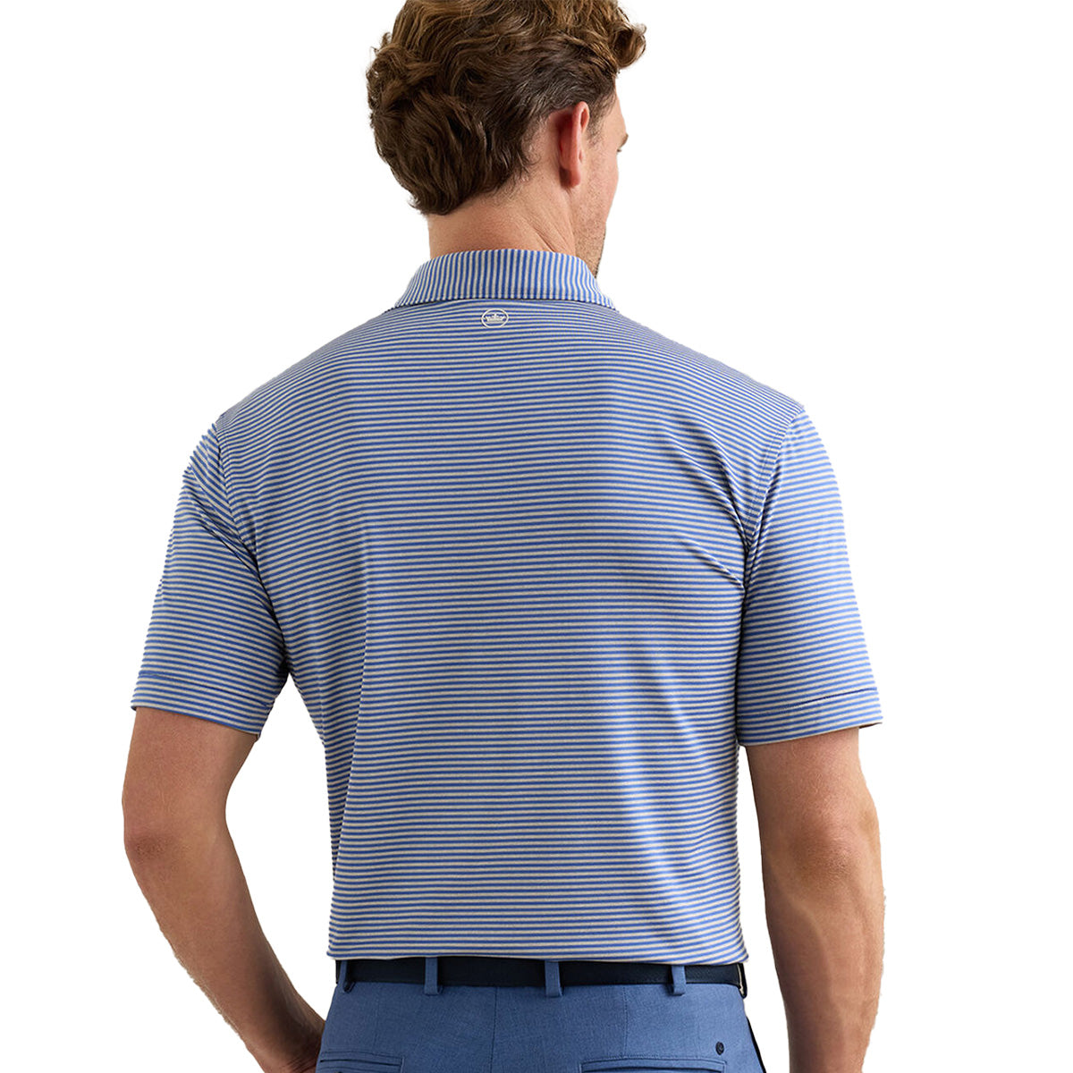 A man is seen from behind wearing a Peter Millar Boeing Men’s Hales Performance Polo in blue and white stripes, tucked into blue pants. This Boeing polo features moisture-wicking fabric and a small logo on the back collar.