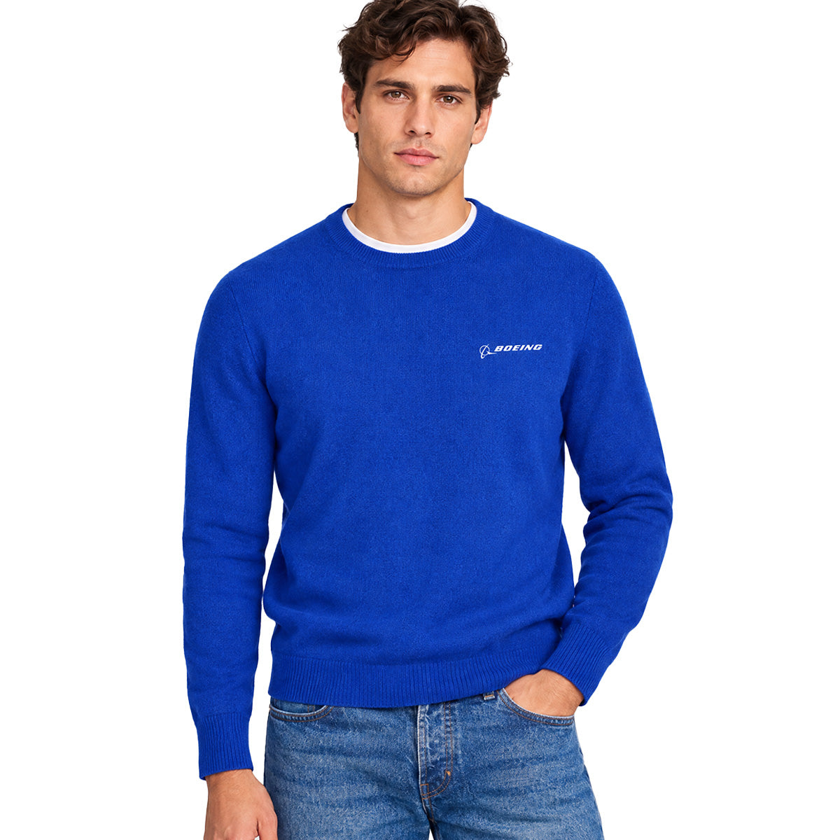 A man is wearing the Boeing Signature Men’s Cashmere Sweater by BOEING in bright blue, layered over a white undershirt and paired with blue jeans. He stands against a plain white background with one hand in his pocket.