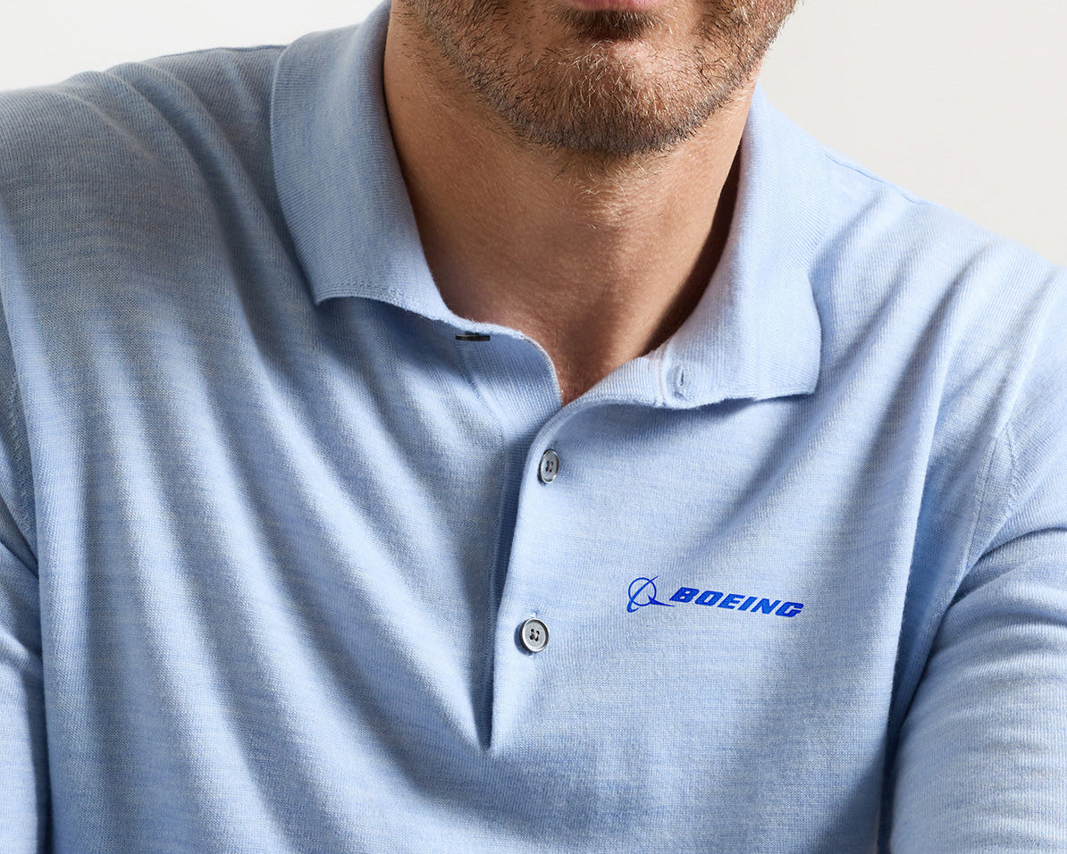 A man is wearing the Peter Millar Boeing Men’s Dorset Sweater Polo, a light blue Merino wool shirt featuring the BOEING logo embroidered on the left chest. His face is partially visible, revealing a neatly trimmed beard and mustache.