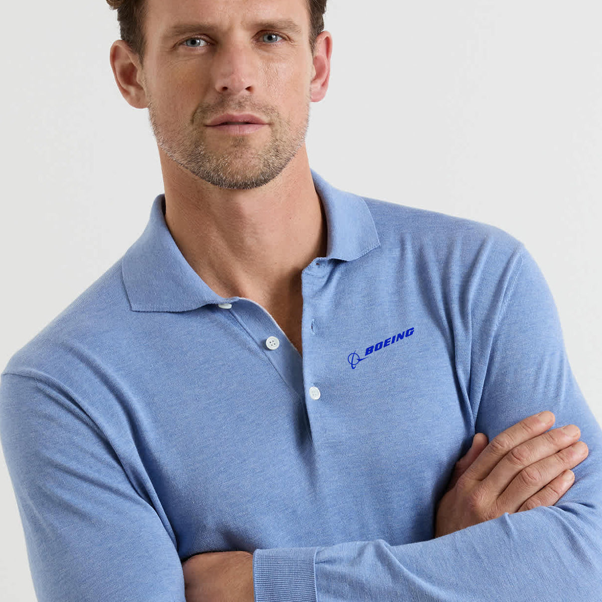 A man with short hair and light stubble wears the Peter Millar Boeing Men’s Dorset Sweater Polo, featuring a Boeing logo on the chest, standing against a plain background with his arms crossed.