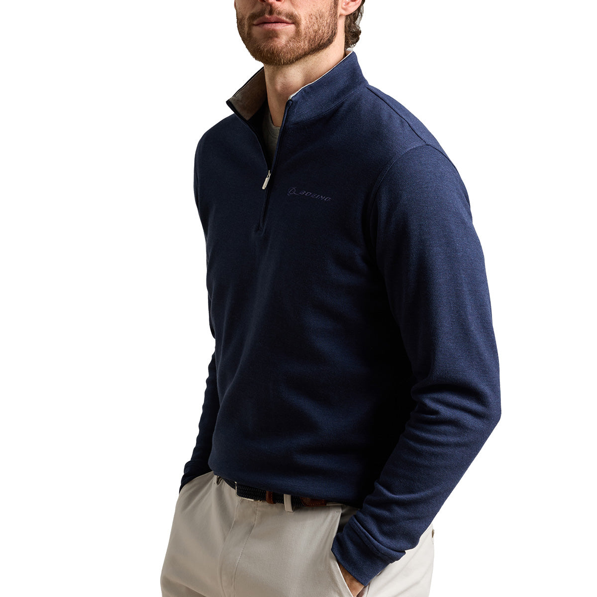 A man wearing the Peter Millar Boeing Men’s Crown Comfort Knit Quarter-Zip in navy and light-colored pants stands with his hands in his pockets against a white background, showcasing the relaxed coastal vibe of this lightweight BOEING sweatshirt layer.