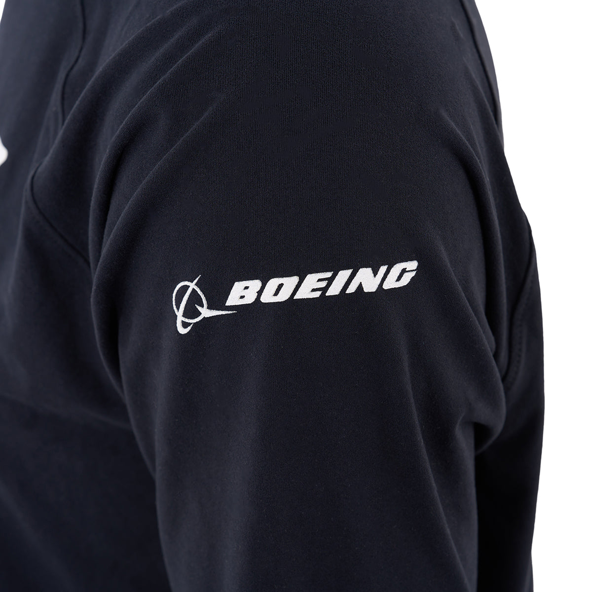 A close-up of a person’s upper arm wearing a black Boeing F-15 Eagle Velocity Unisex Tech Stretch Hoodie by BOEING, featuring the white BOEING logo on the sleeve.