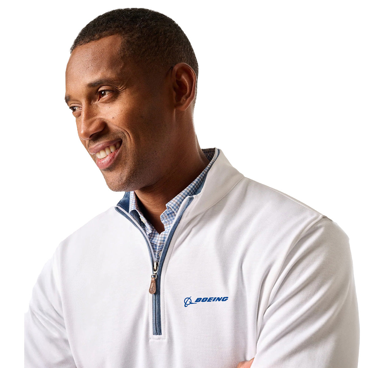 A man smiles and looks to the side, wearing a johnnie-O Boeing Men’s Sully Quarter-Zip over a blue checked shirt. The Boeing logo is visible. He stands against a plain white background.