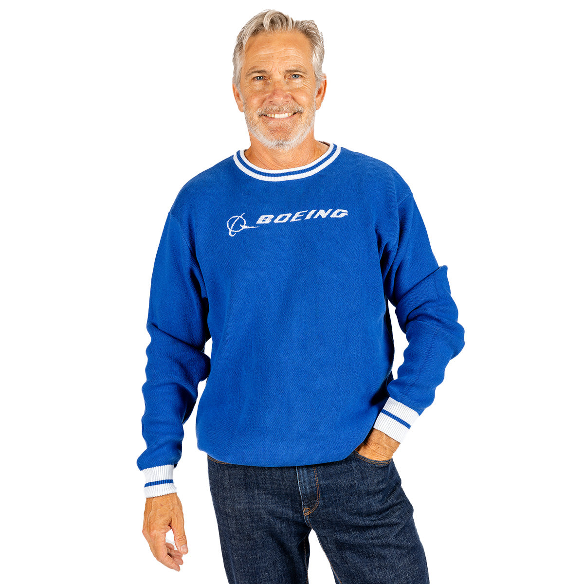A smiling man with gray hair is wearing the Boeing Signature Unisex Andre Crewneck Sweatshirt by BOEING—a premium blue sweater featuring the Boeing logo and white trim—paired with dark jeans, standing against a plain white background.