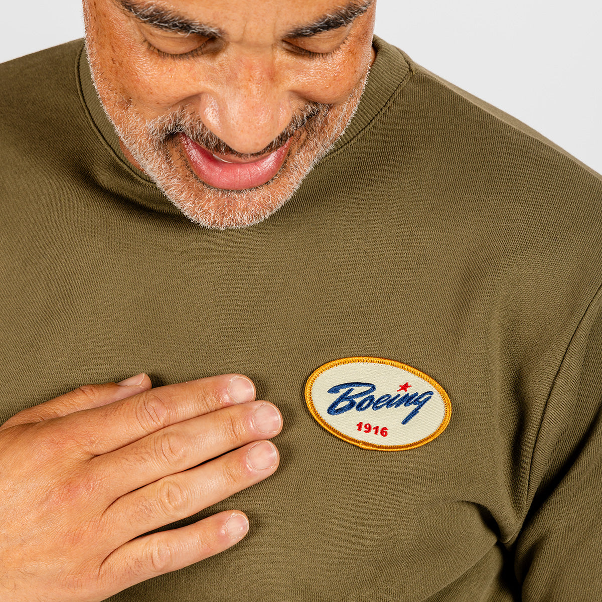 A person smiles while touching a Boeing Heritage Airplane Company Unisex Crewneck Sweatshirt by BOEING, showing only their lower face and hand.