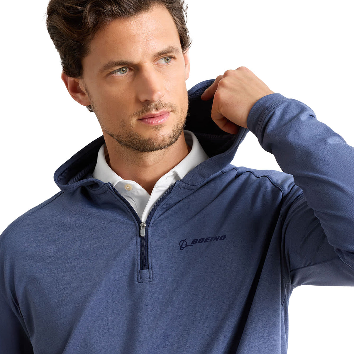 A man with short brown hair and a light beard adjusts the hood of the Peter Millar Boeing Men’s Pine Quarter-Zip Performance Hoodie while looking to the side. This blue quarter-zip hoodie by BOEING is crafted from four-way stretch fabric for ease of movement and features moisture-wicking technology for comfort. The background is plain white.