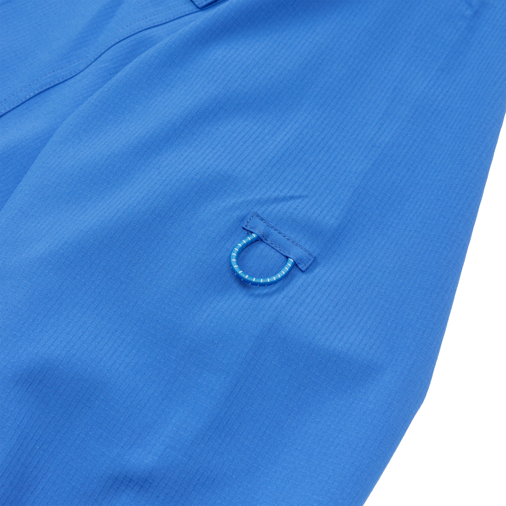 Close-up of blue fabric with a subtle texture and a small blue cord loop, from the BOEING Signature Logo Men's Long Sleeve Utility Shirt. A sewn seam appears at the top, highlighting the shirt's utility design.