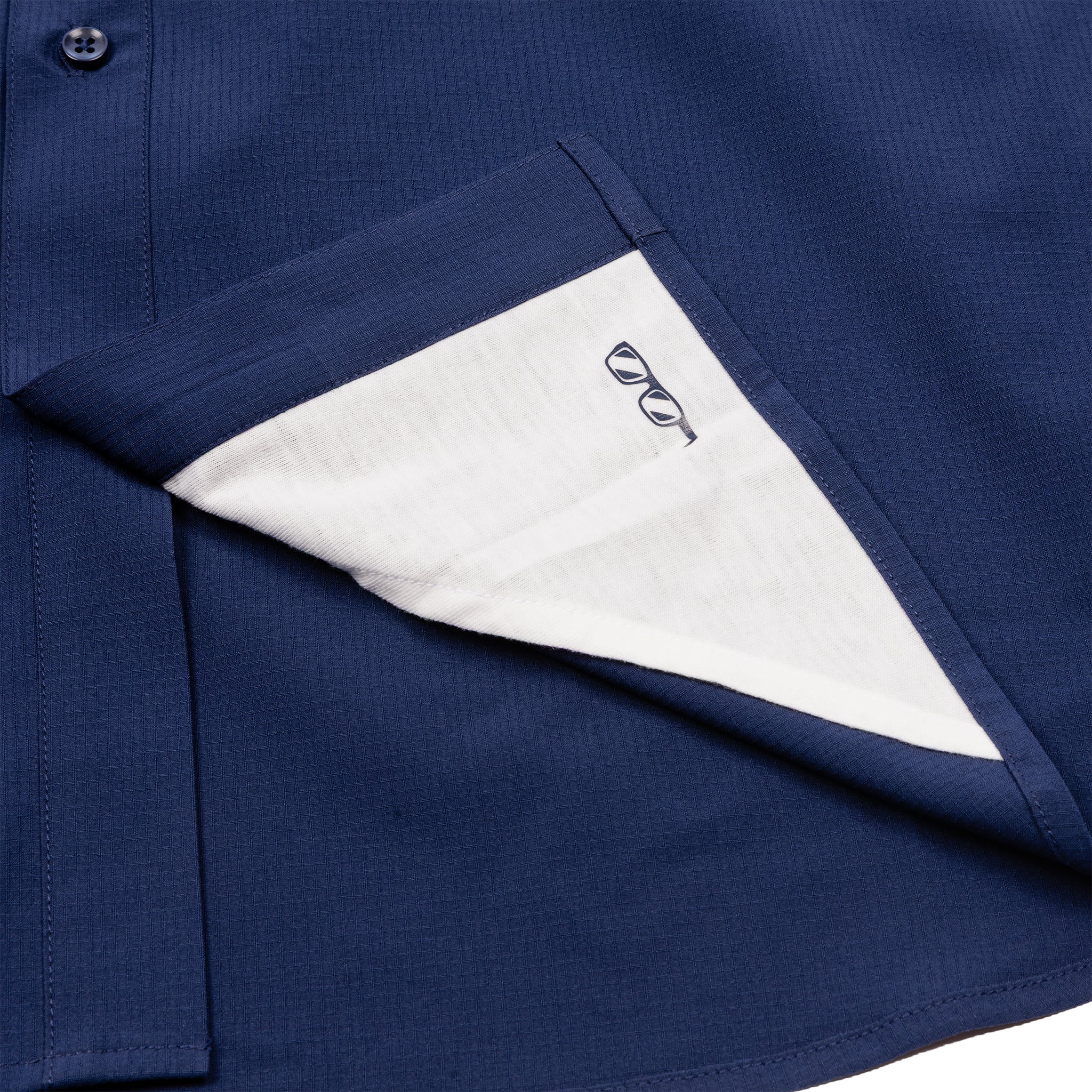 A close-up of the BOEING Signature Logo Men's Short Sleeve Utility Shirt in navy blue, showing the front pocket partially turned inside out to reveal a white lining with a small black eyeglasses embroidery.