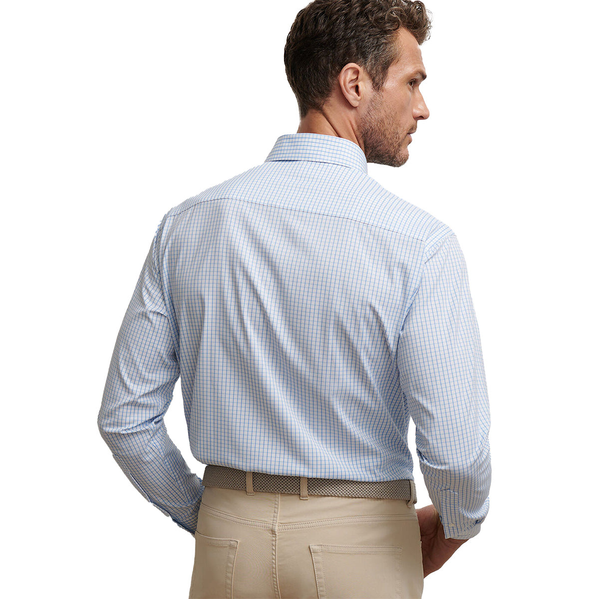 A man with short, curly brown hair is seen from the back in a light blue checkered Peter Millar Boeing Men’s Hanford Twill Sport Shirt and beige pants with a woven belt, standing against a white background.