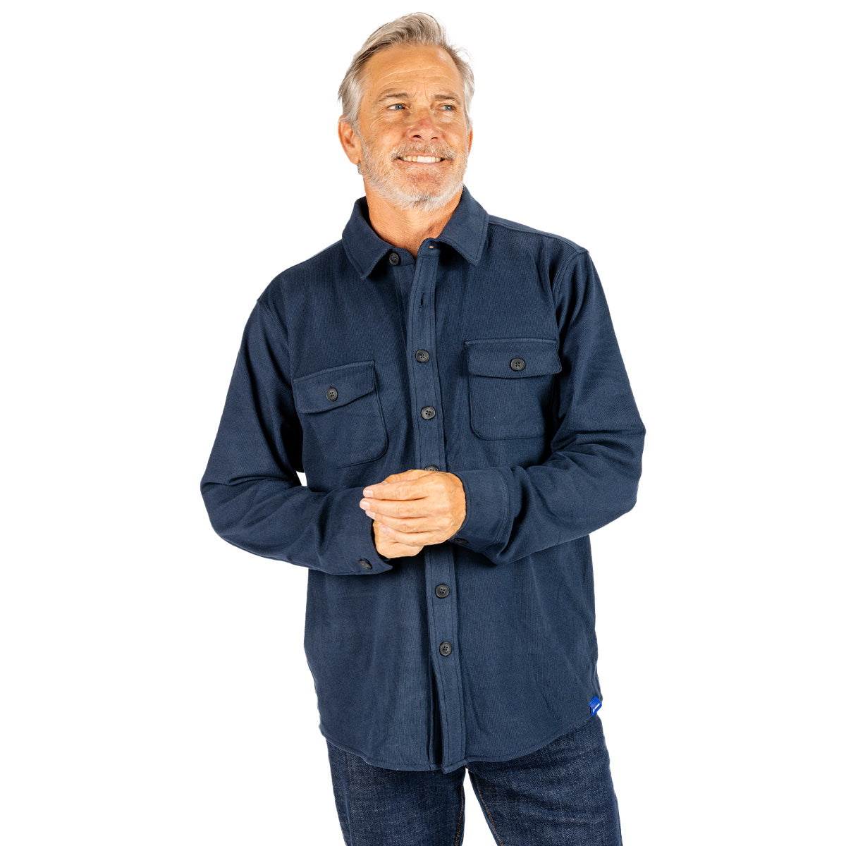 A smiling older man with gray hair and a beard wears the Boeing Unisex Journey Overshirt by BOEING, featuring two chest pockets, while standing against a white background.