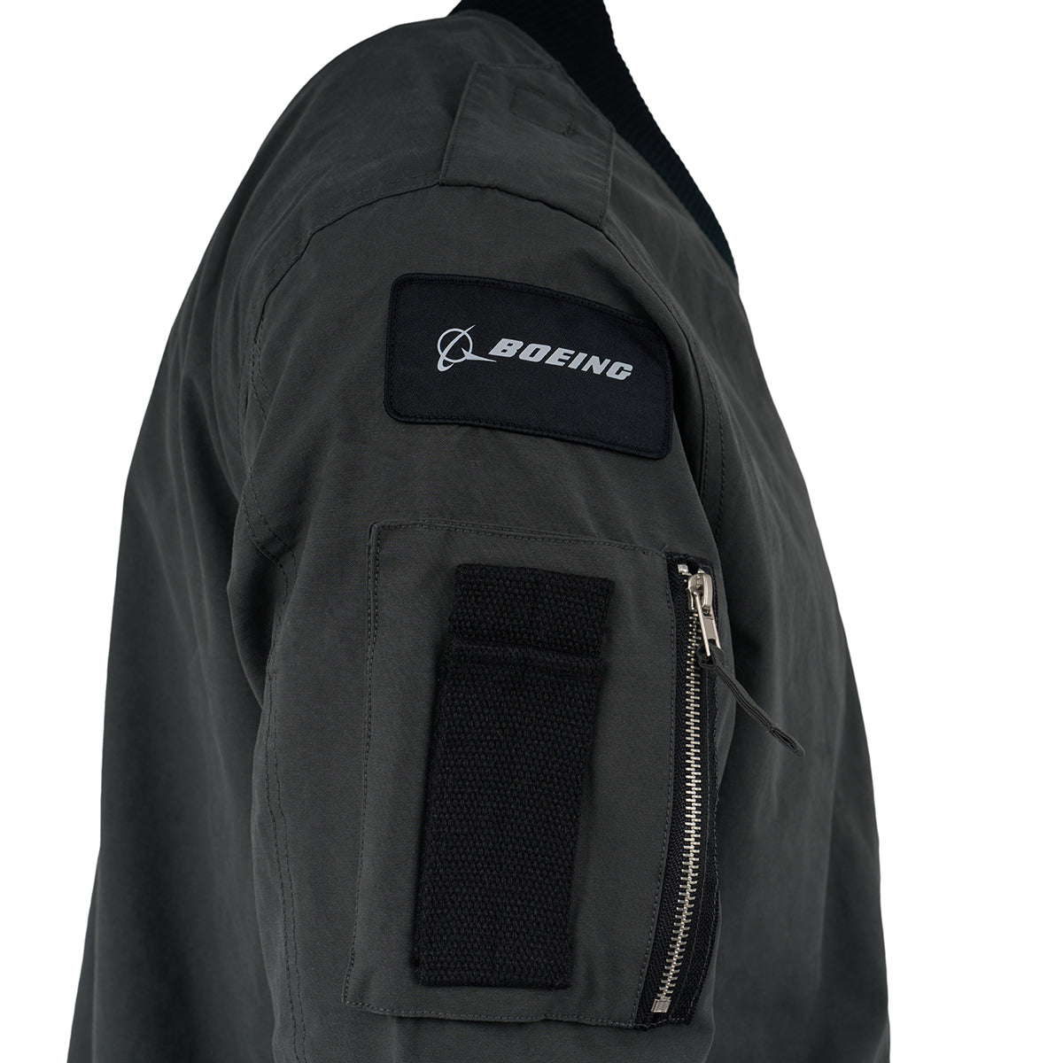 A close-up of a dark green Red Canoe Boeing Flight Jacket sleeve from The Boeing Store shows a zippered pocket, black Velcro patch, and a black patch with the white Boeing logo.