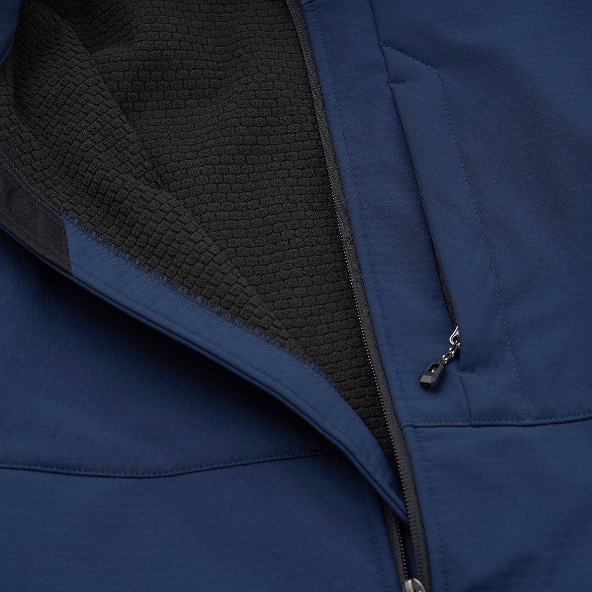 Close-up of the BOEING Men's Softshell Jacket in blue, with a partially unzipped front showing a black honeycomb-patterned lining and a zippered chest pocket. This wind-resistant jacket combines style with function.